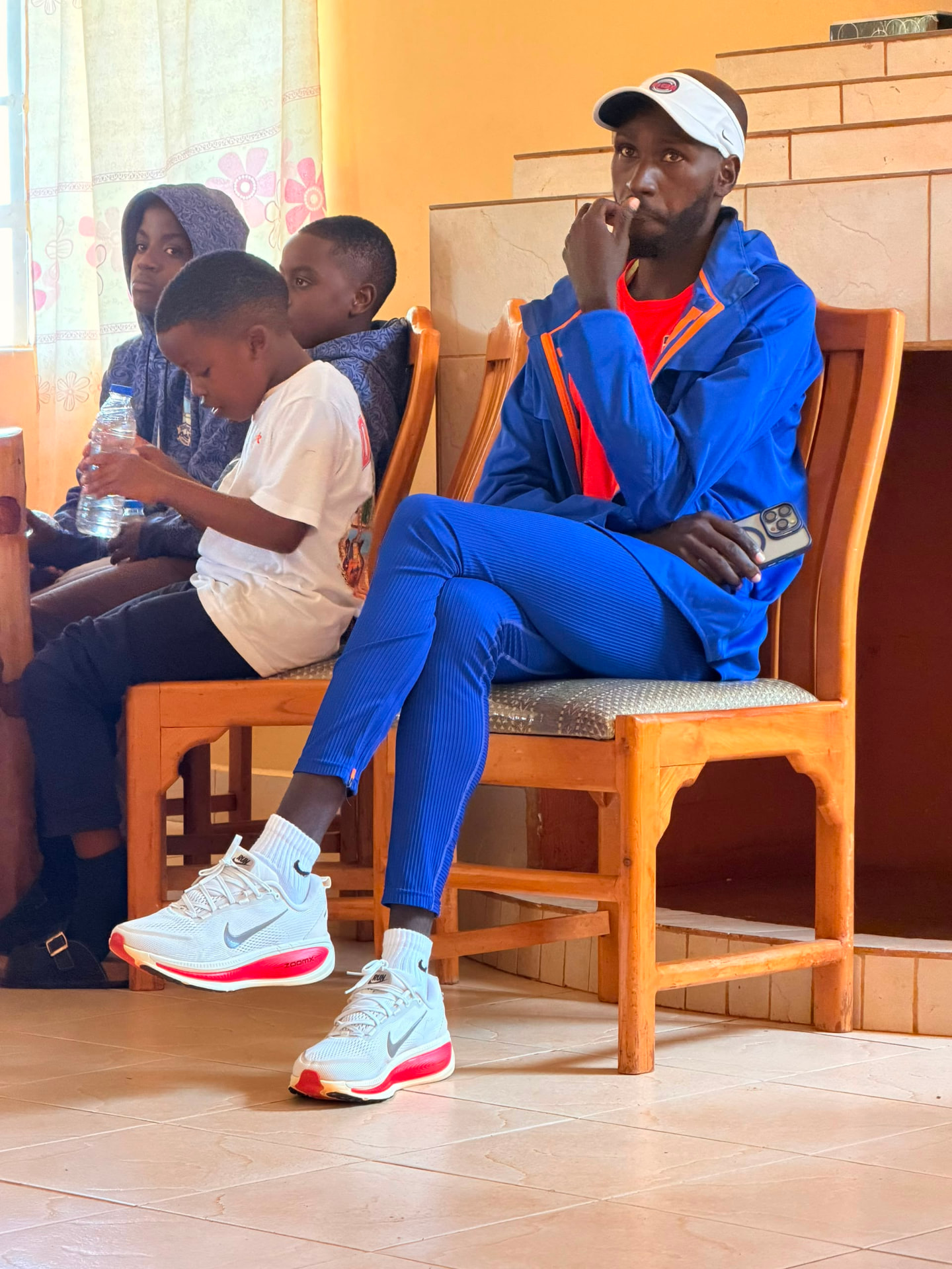 Academy coach in a blue tracksuit seated with young players during an indoor session